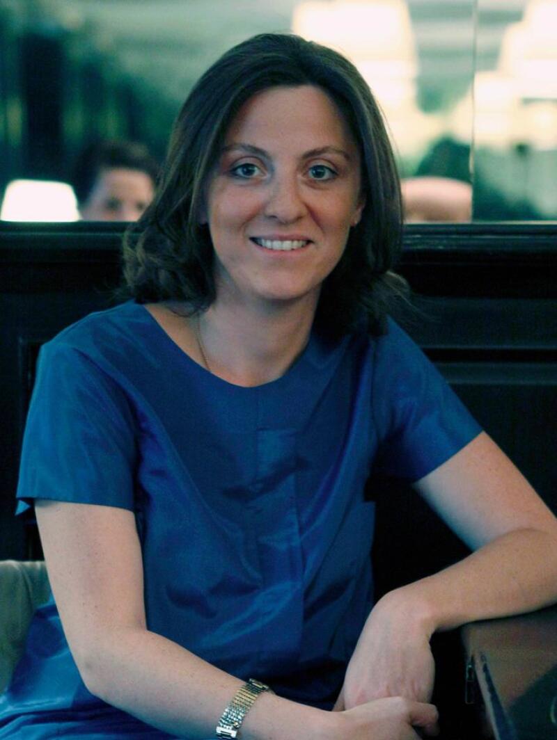 A woman with brown hair and blue eyes is wearing a blue shirt and a watch.