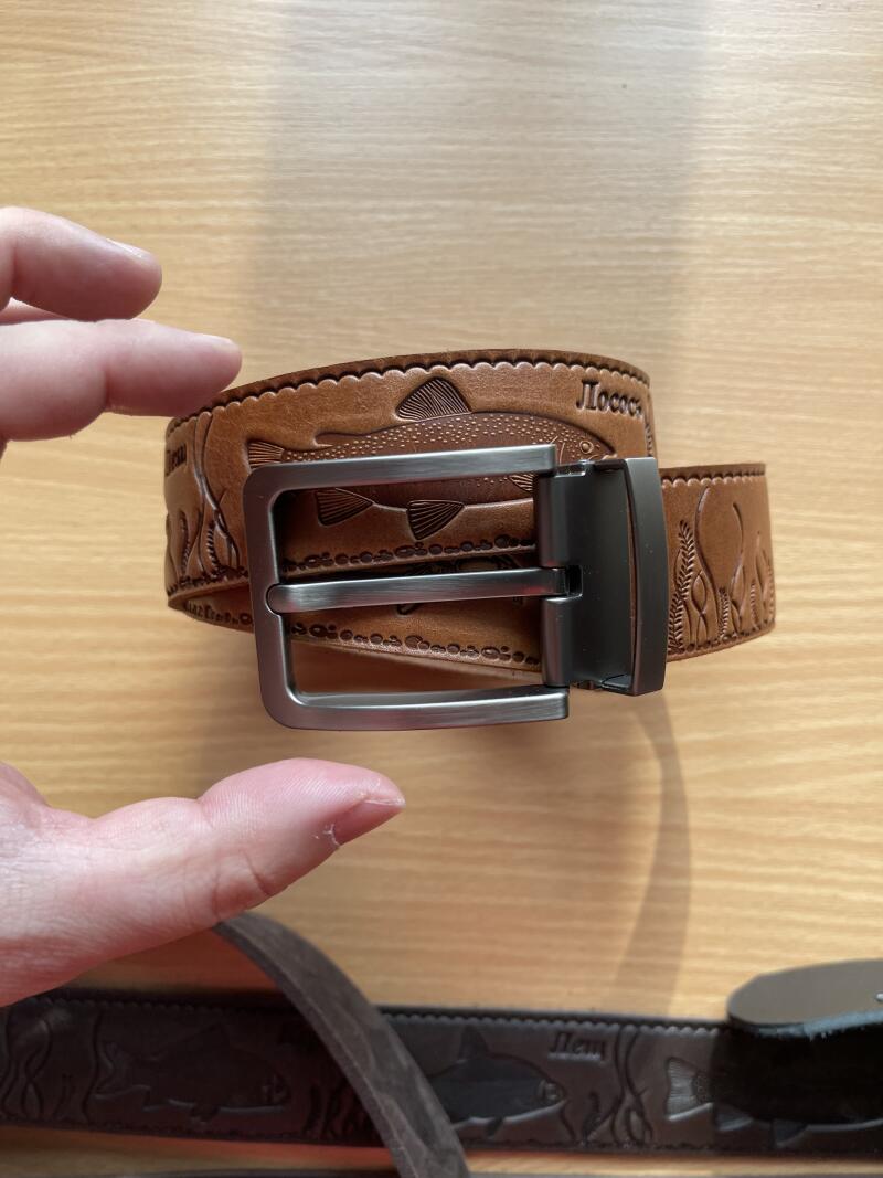 A brown leather belt with a silver buckle is decorated with embossed fish and the word "Лосось" (Salmon) in Russian.