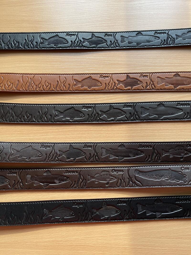 Several belts with fish patterns, including carp, bream, salmon, perch, and catfish, are laid out on a wooden surface, with the names of the fish embossed next to their respective images.