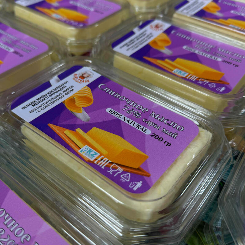 Packaged butter with a purple label that reads "Сливочное масло 72% сары май 100% NATURAL 200 гр" in Russian and English, along with an image of butter curls and a wedge.