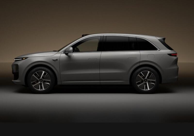 A gray SUV is parked on a gray surface against a tan background.