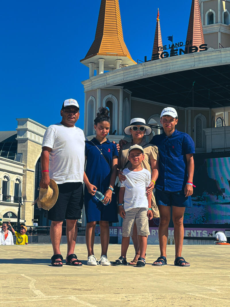 A group of five people are standing in front of a building that reads "THE LAND OF LEGENDS"; the group consists of two men, one woman, one girl, and one boy, all casually dressed and looking at the camera.