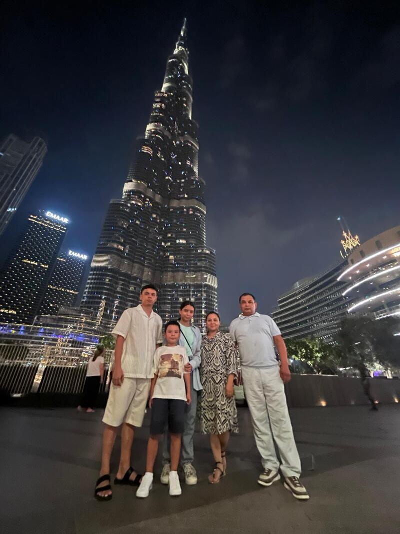 A family of five poses in front of the Burj Khalifa at night; the skyscraper is lit up, and the sky is dark.