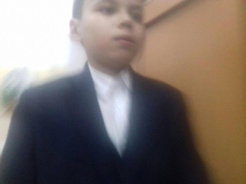 A boy in a dark jacket and white shirt looks upwards.