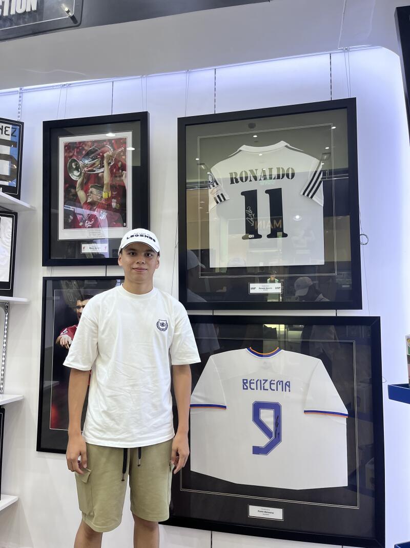 A young man stands in front of framed jerseys of soccer players Ronaldo and Benzema.