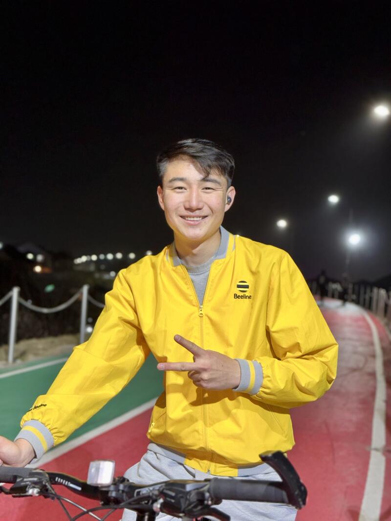 A man in a yellow "Beeline" jacket gives a peace sign while sitting on a bicycle at night.