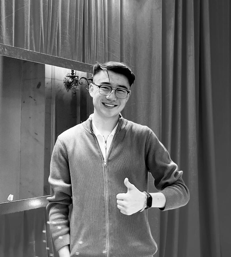 A grayscale shot features a smiling man in glasses and a zip-up sweater, giving a thumbs-up in front of a curtained backdrop.