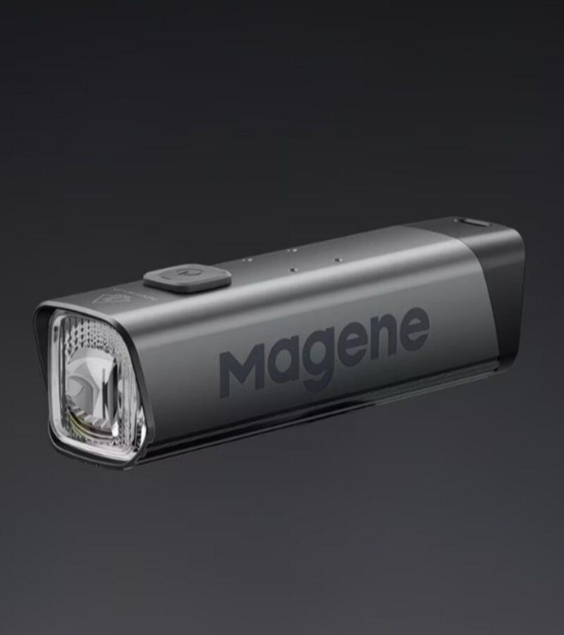 A dark grey bicycle headlight with a clear lens and a button on top, displaying "Magene" on its side, set against a dark grey background.