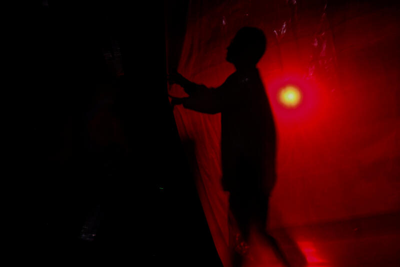 Силуэт человека, отодвигающего занавес под красным освещением.