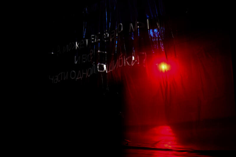 На изображении представлена темная сцена с текстом на русском языке, который гласит: «А может, в этом мире я всего лишь часть одной ошибки?» и красным источником света, освещающим драпированную поверхность.