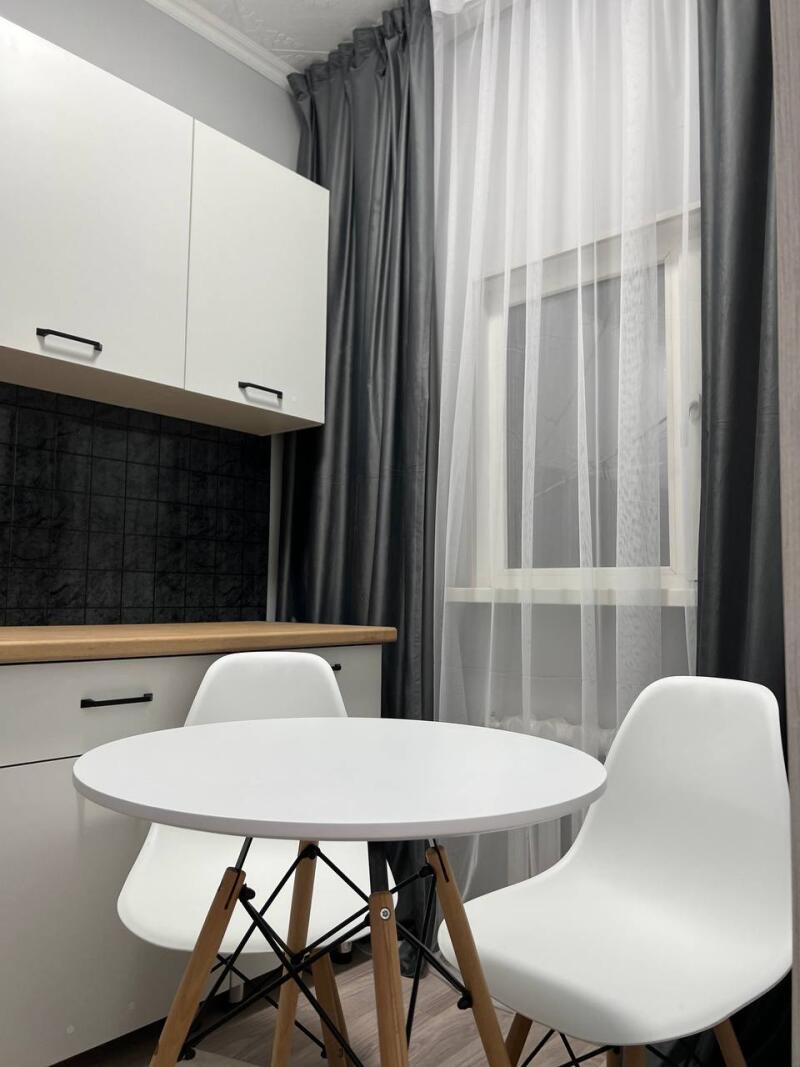 The image shows a kitchen interior with a white round table and chairs, white cabinets, and gray curtains.