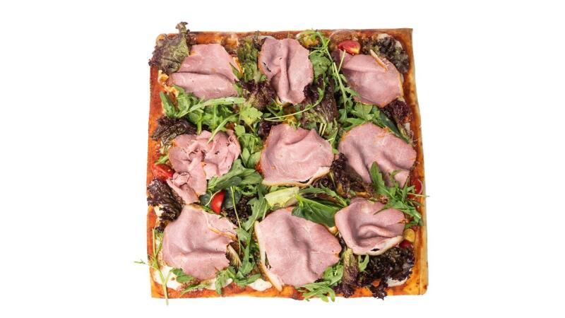 Квадратная пицца с ломтиками ветчины, рукколой и темной зеленью.