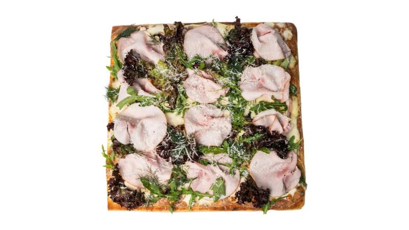 Квадратная пицца с ломтиками мяса, зеленью и тертым сыром на белом фоне.