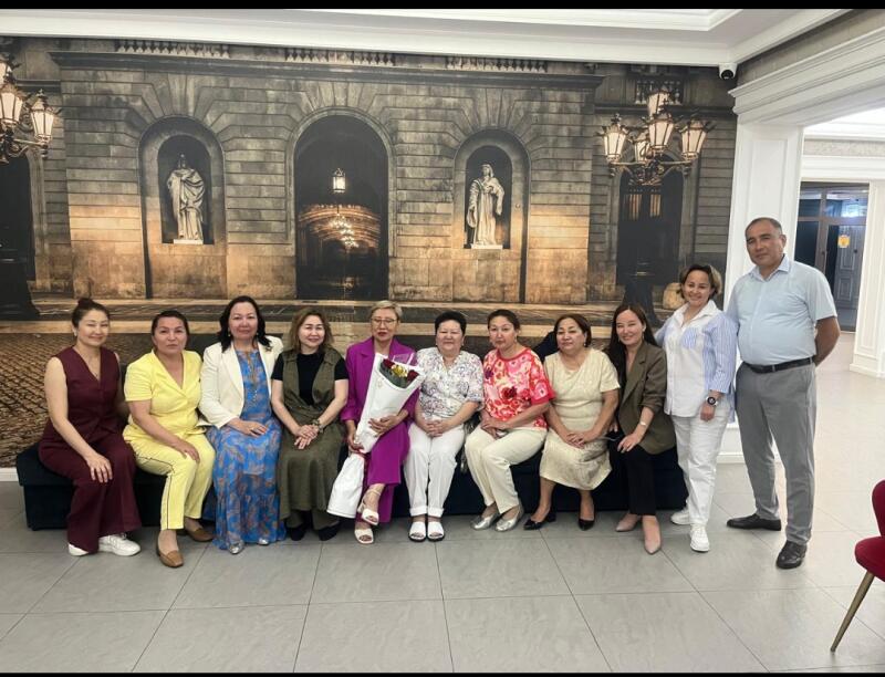 A group of eleven people, ten women and one man, are posing for a photo in a brightly lit room with a large mural behind them.