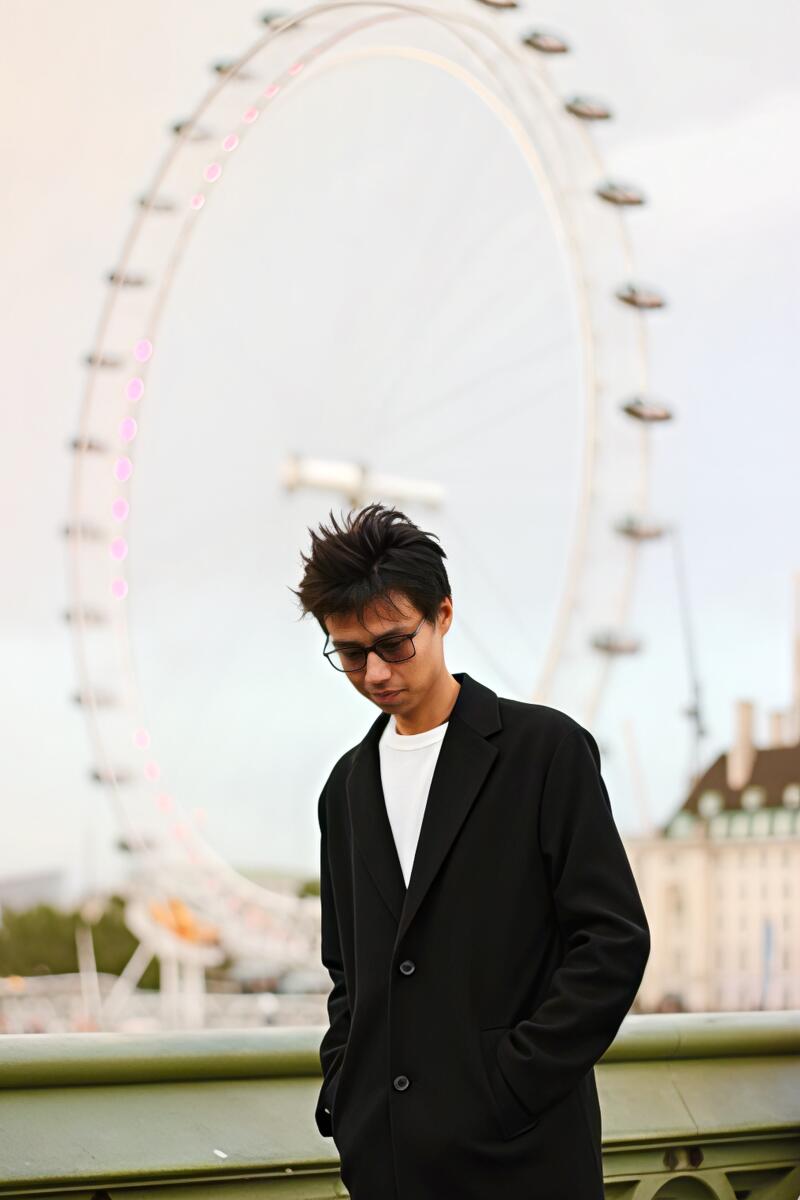 A man in glasses and a black coat stands in front of the London Eye.