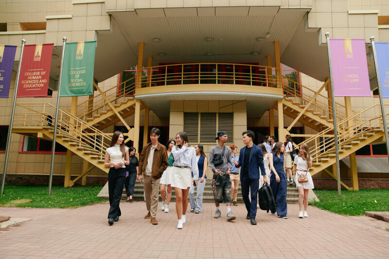A group of students walks in front of a building with banners that read "COLLEGE OF HUMAN SCIENCES AND EDUCATION", "COLLEGE OF SOCIAL SCIENCES", and "SCHOOL OF LAW".
