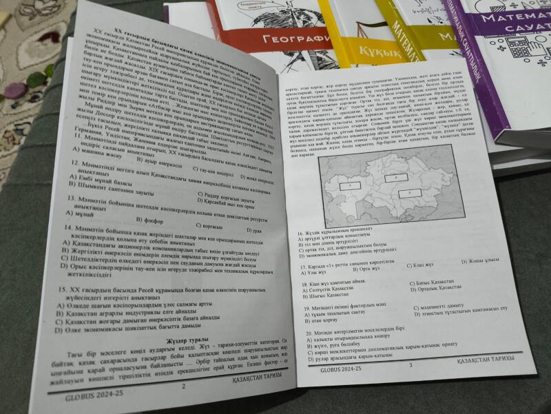 На изображении открытые страницы учебника "Kazakhstan Tarihi" от GLOBUS 2024-25, с текстом на казахском языке и вопросами с несколькими вариантами ответов, рядом с учебниками с надписями "География", "Кукык" и "Matematikalyk Sauattylyk."