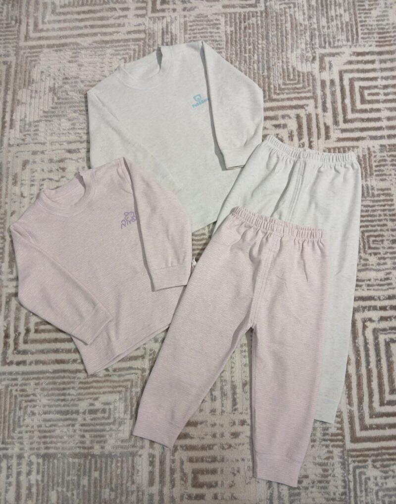 The image shows two sets of children's thermal underwear, one in light pink and the other in light gray, laid out on a patterned rug.
