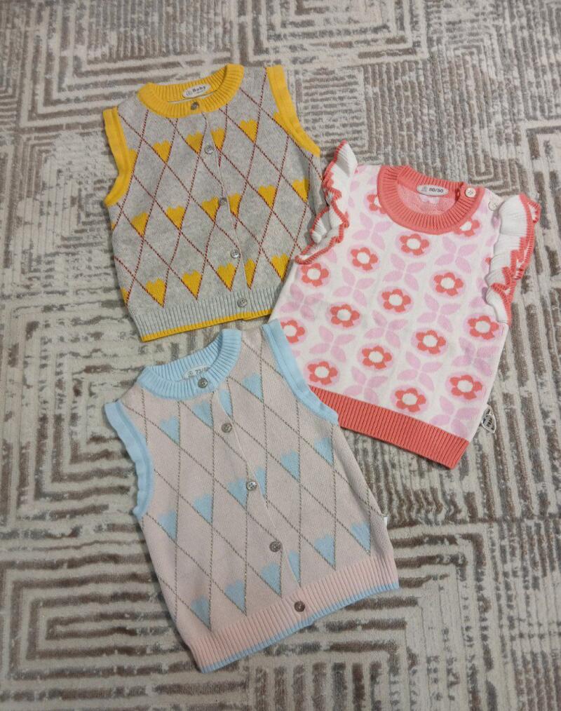 The image shows three baby vests with different patterns and colors, laid out on a patterned surface.