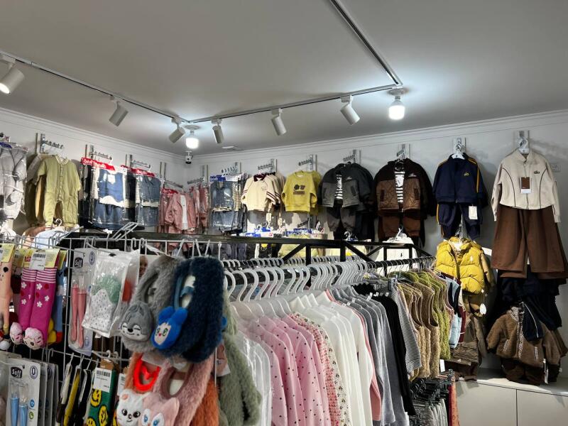 The photograph shows a retail store with clothing racks and wall displays filled with a variety of garments, including jackets, pants, and shirts in different colors and styles, under track lighting.