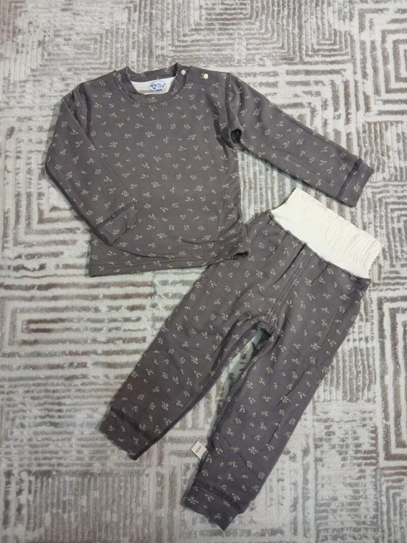 A gray long-sleeved shirt with buttons on the shoulder and matching pants with a white waist band are laid out on a patterned rug.