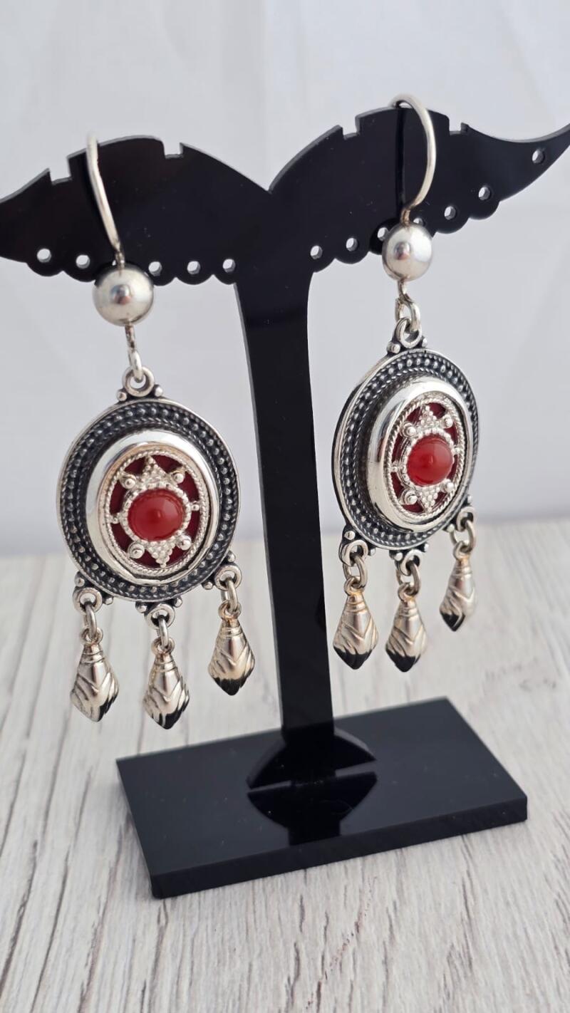 Two silver earrings with red gemstones are displayed on a black jewelry stand against a white background.