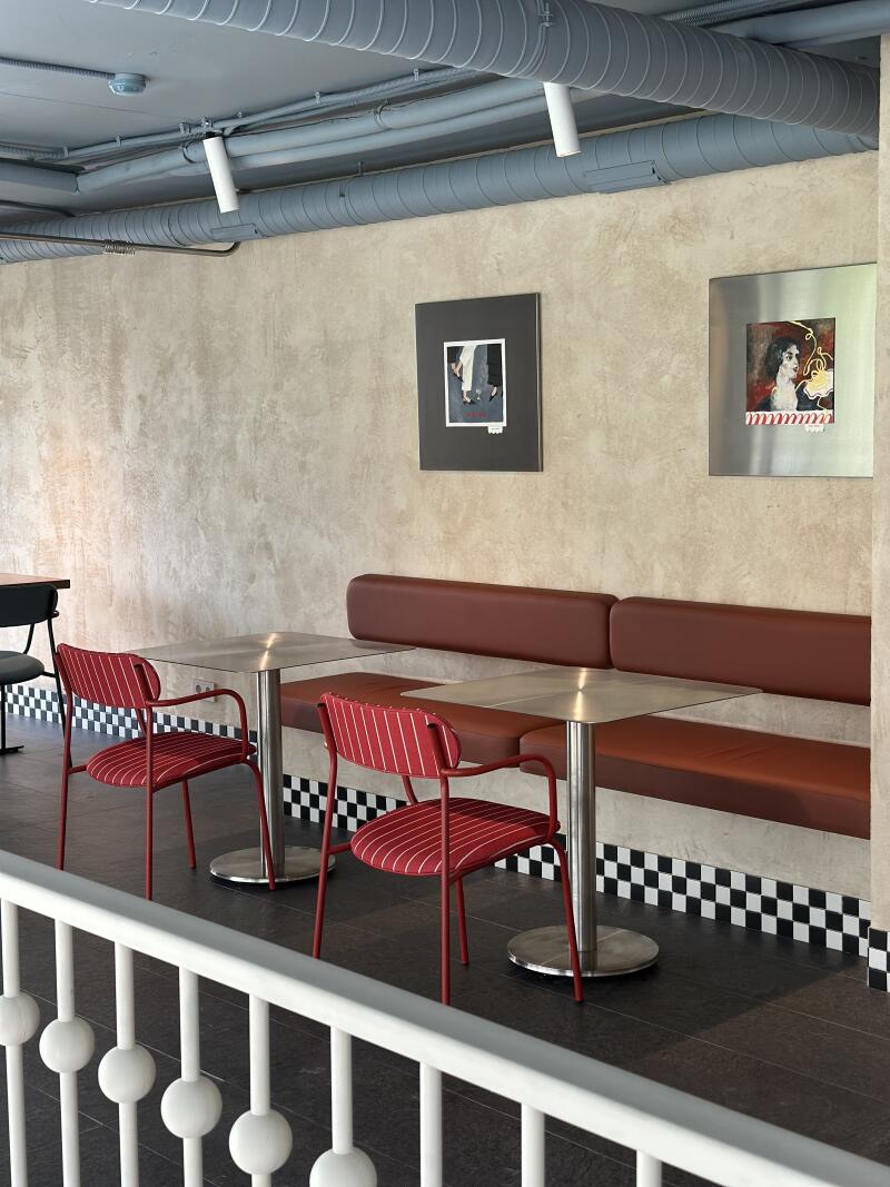 The photo shows a restaurant interior with two red and white striped chairs, a built-in brown leather bench, stainless steel tables, and two framed pictures on the wall.