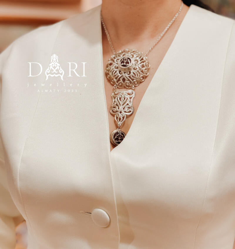 A person wears a white jacket and a silver necklace with intricate designs and dark stones; the logo for "DARI jewellery ALMATY 2025" is visible on the left.