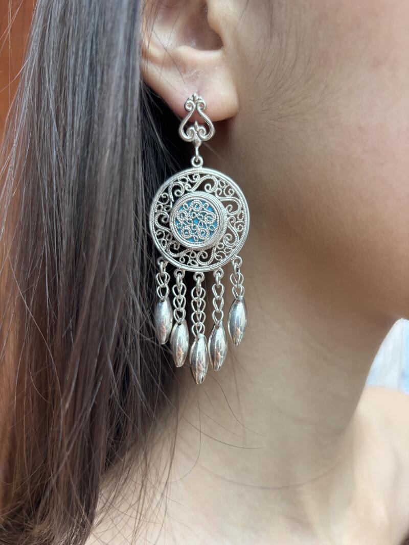 A close-up shot shows a woman wearing a silver earring with a blue center and dangling silver pendants.