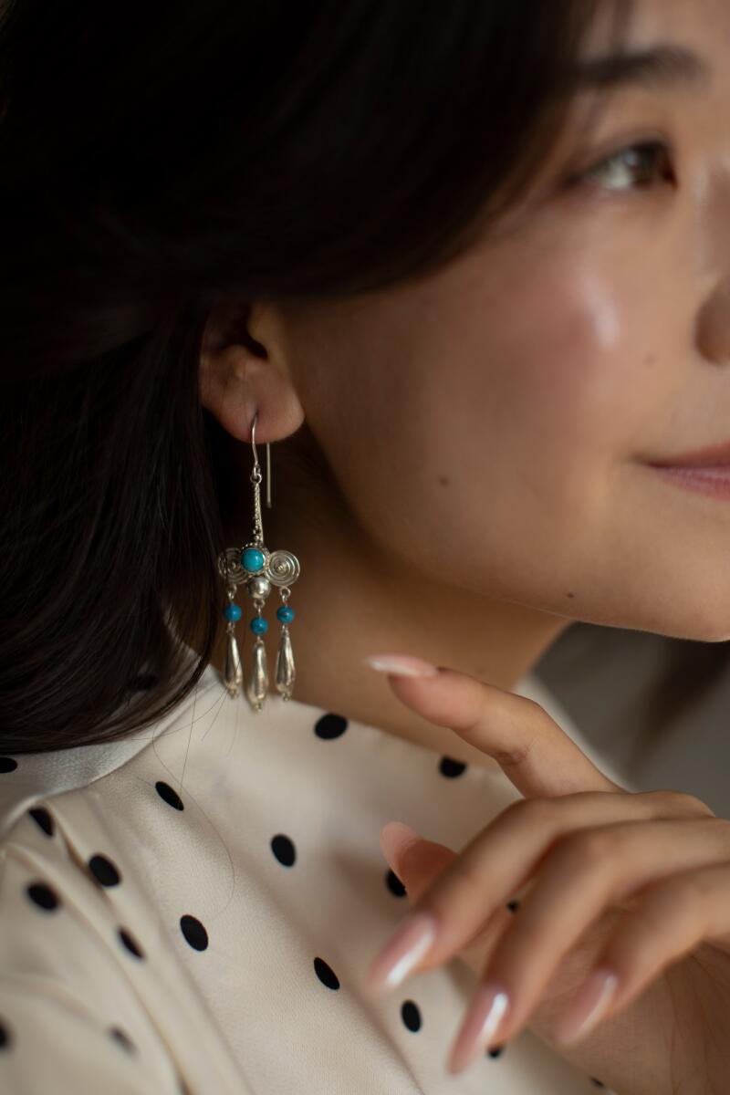 A woman is wearing a silver earring with turquoise stones and a white polka dot shirt.