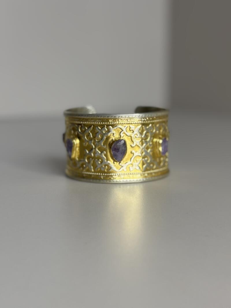 The image shows a silver and gold cuff bracelet adorned with purple gemstones.
