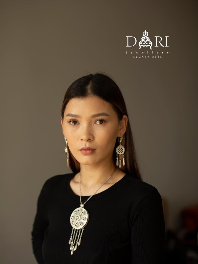 A woman with long brown hair is wearing a black shirt and silver jewelry, including a necklace and earrings; the logo "DARI jewellery ALMATY 2025" is visible above her head.