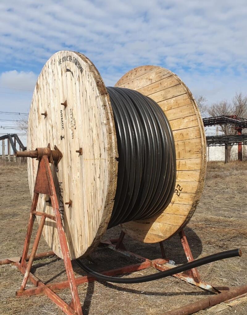 A large wooden spool of black cable sits on a rusty metal stand outdoors.