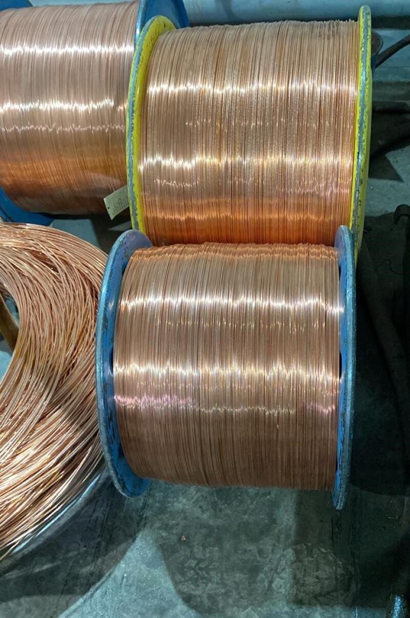 The image shows several spools of copper wire, some still wound tightly on their spools, others loose and coiled.