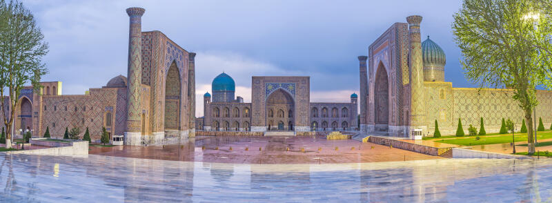 The photo shows a panoramic view of a square and buildings in Samarkand, Uzbekistan, featuring ornate facades and blue domes.