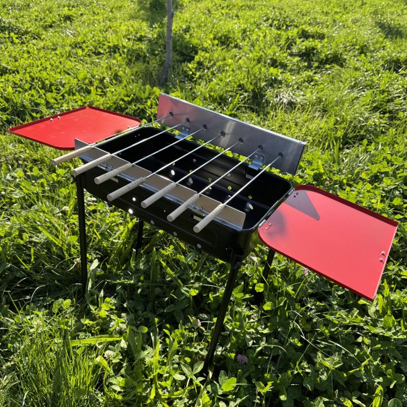 A black mangal with metal skewers and red side tables stands on the grass.