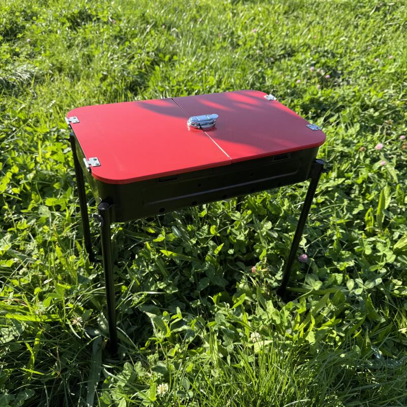 A portable red and black grill stands on a grassy lawn.
