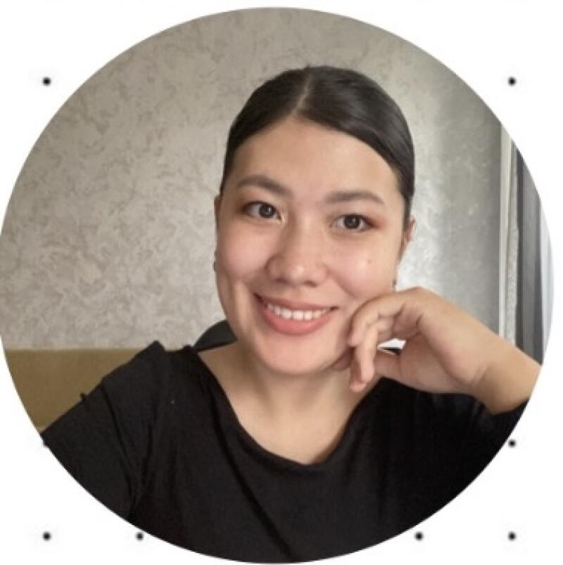 A smiling woman with dark hair pulled back is posing with her hand on her face, wearing a black shirt in a circular frame.