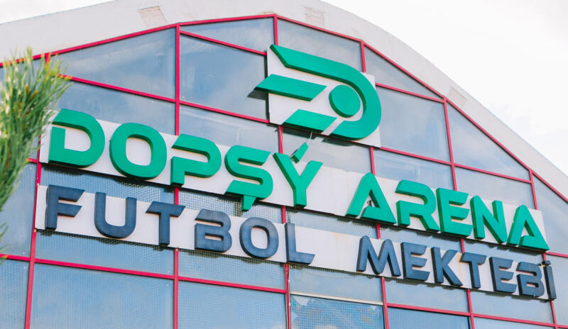 Exterior shot of a building with a sign that reads "DOPSY ARENA FUTBOL MEKTEBI" in green and dark gray letters.