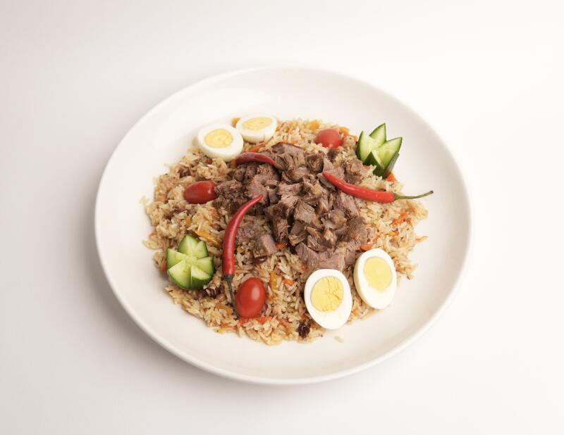 Тарелка плова с мясом, украшенная яйцами, огурцами, помидорами и перцем чили.
