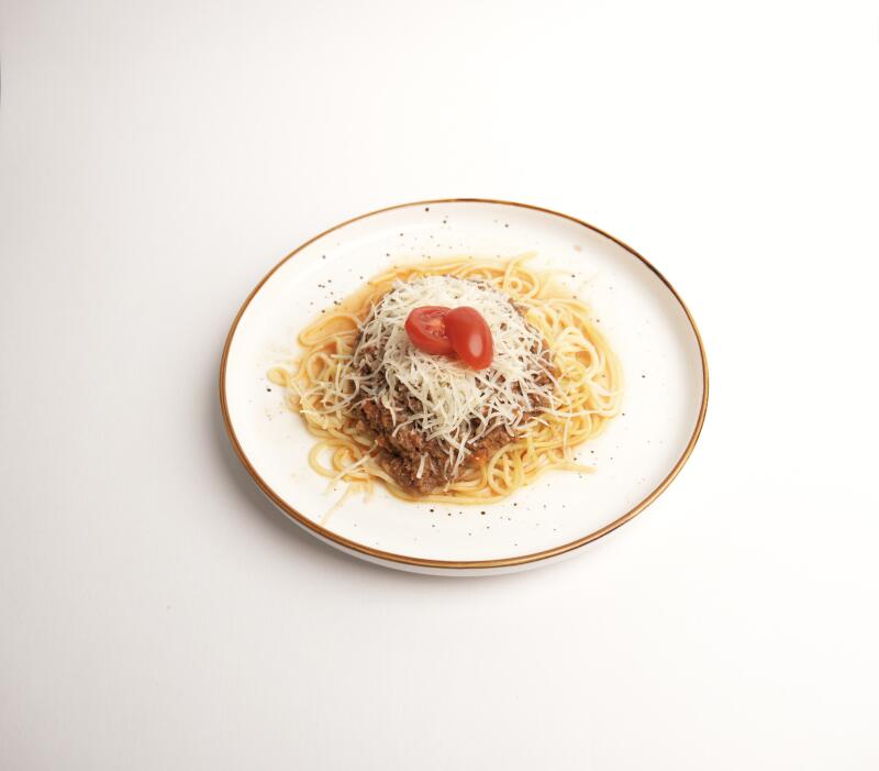 Тарелка спагетти с мясным соусом, посыпанная тертым сыром и двумя половинками помидоров черри.