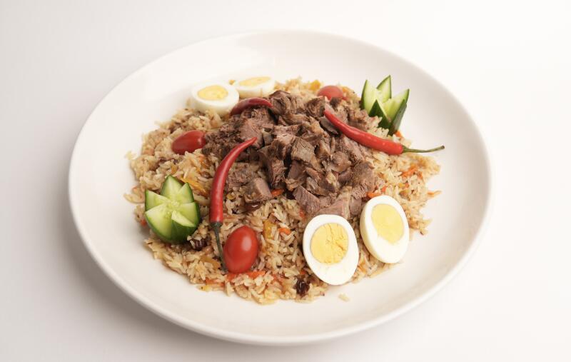 Тарелка плова с мясом, яйцами, перцем чили, огурцами и помидорами.
