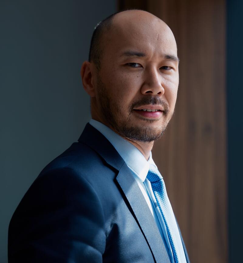A portrait of a bald man with a beard, wearing a blue suit and light blue tie.