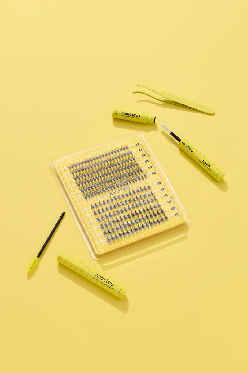 The image shows a set of individual false eyelashes in a clear plastic case, surrounded by eyelash application tools, all set against a yellow background; the products include tubes and brushes labeled with the brand name "Mattey" and Russian text such as "ФИКСАТОР" (Fixative) and "КЛЕЙ" (Glue).