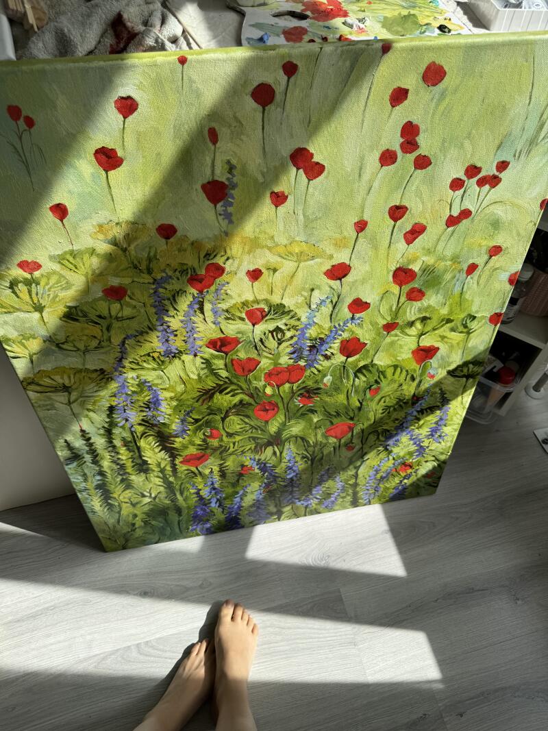 На изображении картина с красными маками и синими полевыми цветами на зеленом фоне, на переднем плане видны ступни ног.