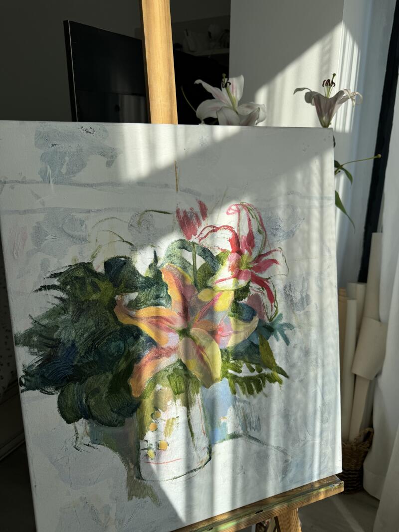 Импрессионистская картина с изображением лилий в вазе стоит на деревянном мольберте в залитой солнцем комнате.