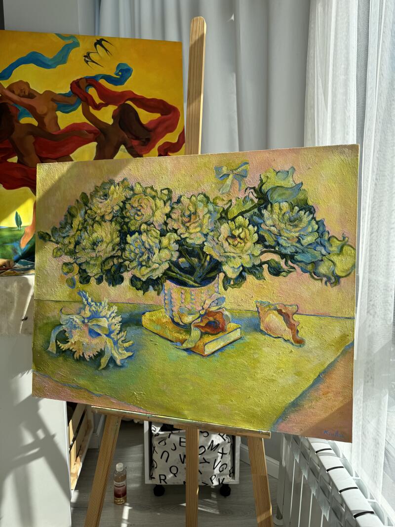 Натюрморт на мольберте изображает букет белых и зеленых цветов в вазе, с ракушками и книгой на зеленой поверхности.