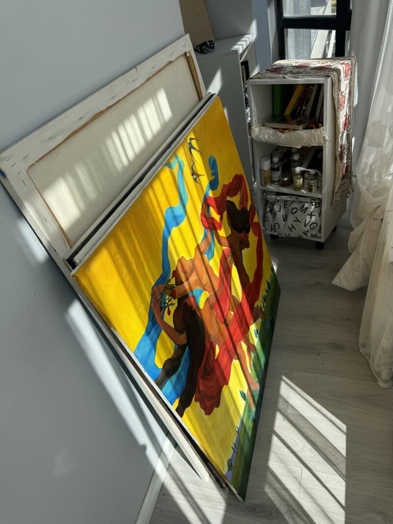 На изображении картина с фигурами и ярко-желтым фоном, прислоненная к стене, рядом с небольшой белой полкой.