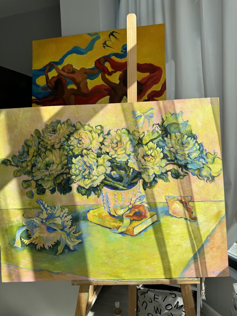 На изображении натюрморт с цветами в вазе, стоящий на мольберте, с другой картиной на заднем плане с изображением фигур и лент.