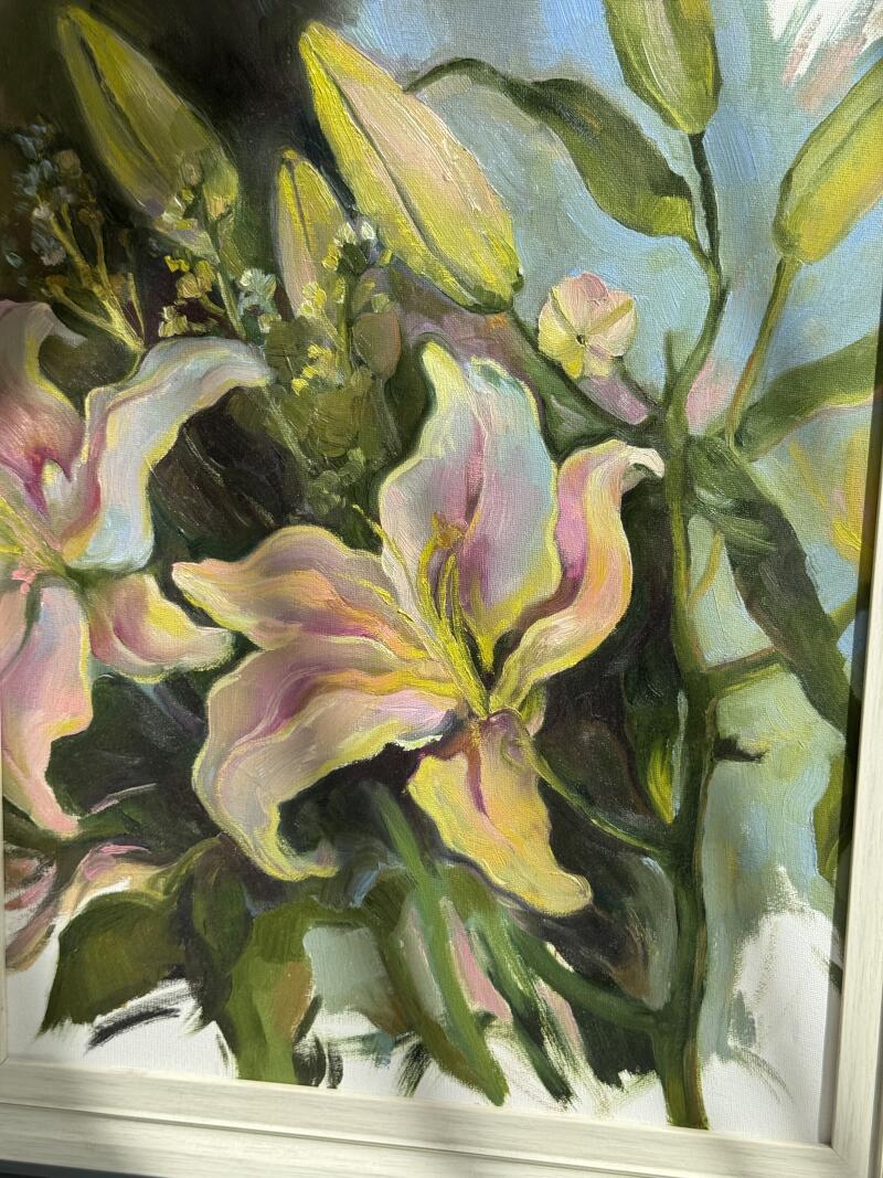 На картине маслом в раме изображены светло-розовые лилии с желтыми оттенками, а также зеленые стебли и бутоны на светло-голубом фоне.